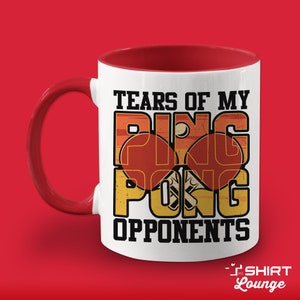 May include: White ceramic coffee mug with a red interior and handle. The mug features a graphic of two ping pong paddles and a ball with the text "Tears of my Ping Pong Opponents".