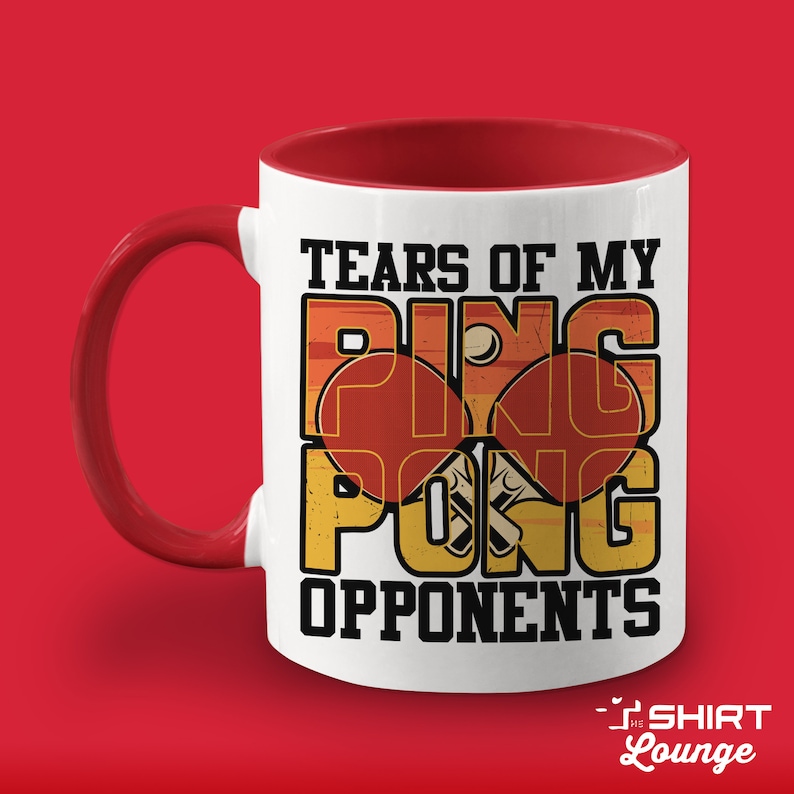 May include: White ceramic coffee mug with a red interior and handle. The mug features a graphic of two ping pong paddles and a ball with the text "Tears of my Ping Pong Opponents".