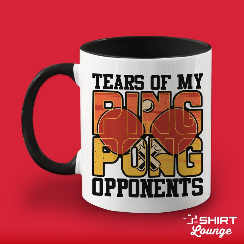May include: White ceramic coffee mug with a black handle and black interior. The mug features a graphic design of two ping pong paddles and a ball with the text "Tears of my Ping Pong Opponents".