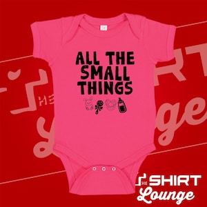 May include: A bright pink baby bodysuit with the text "ALL THE SMALL THINGS" in black. Below the text are black illustrations of a bunny, rattle, pacifier, and bottle. The bodysuit has short sleeves and three snaps at the bottom.