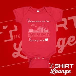 May include: Red baby onesie with a white outline of the Kansas City skyline and the text "Someone in Kansas City loves me" with a white heart.
