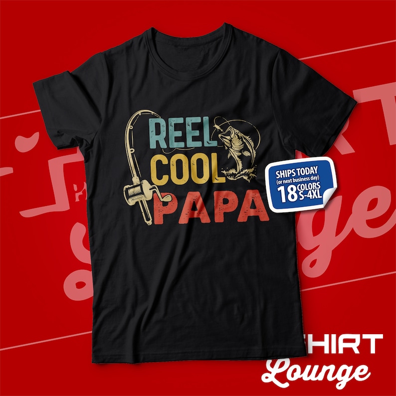 以下が含まれることがあります： 「Reel Cool Papa」というテキストと、ヴィンテージスタイルの釣り竿と魚のグラフィックがプリントされた黒いTシャツです。