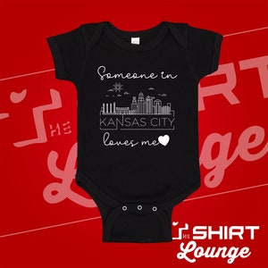 May include: Black baby onesie with a white graphic of the Kansas City skyline and the text "Someone in Kansas City loves me".