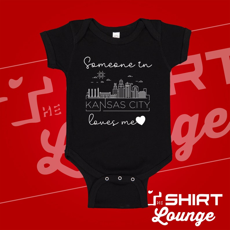 May include: Black baby onesie with a white graphic of the Kansas City skyline and the text "Someone in Kansas City loves me".