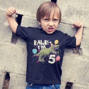 May include: A black t-shirt with a green dinosaur wearing a party hat and the text "Rawr! I'm 5" with colorful confetti and balloons.