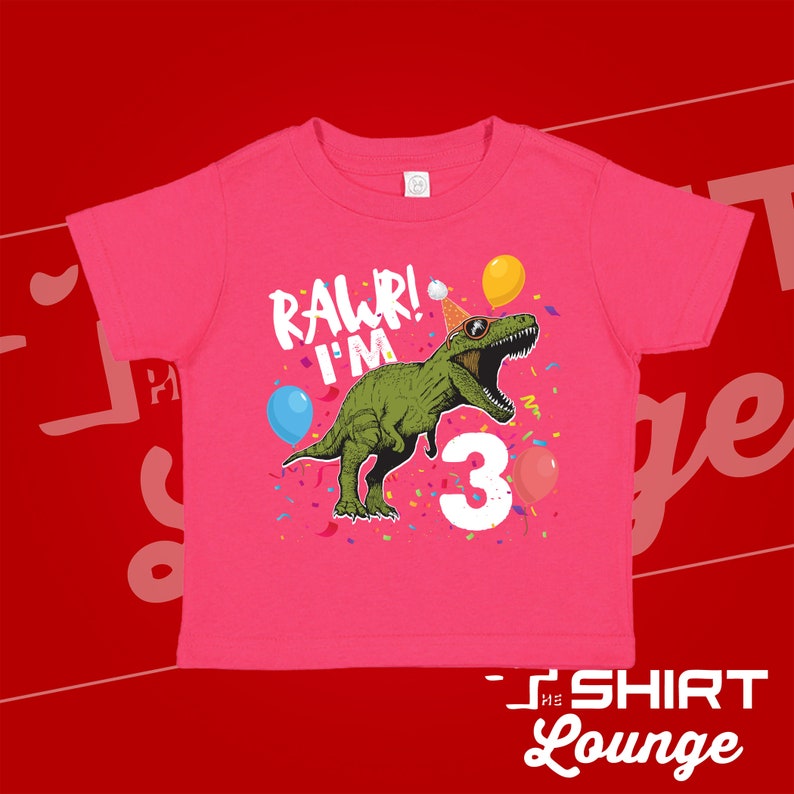 May include: Pink t-shirt with a green dinosaur wearing a party hat and sunglasses. The dinosaur is saying "Rawr! I'm 3" with confetti and balloons around it.