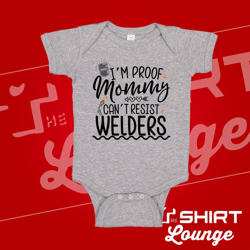 May include: Gray baby onesie with a black graphic that reads "I'm proof mommy can't resist welders". The graphic includes a welding mask, a welding torch, and hearts.