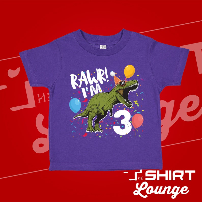 May include: Purple short-sleeved t-shirt with a green dinosaur wearing a party hat and sunglasses. The dinosaur is surrounded by confetti and balloons. The text "RAWR! I'M 3" is printed on the shirt.