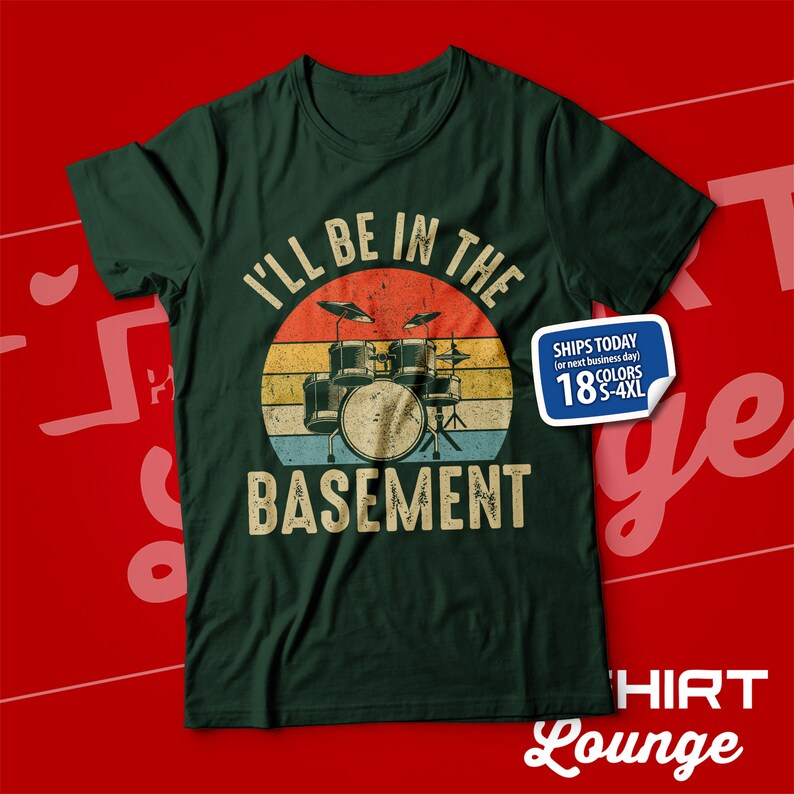 May include: Green t-shirt featuring a vintage-style graphic of a drum set and the text "I'll be in the basement".
