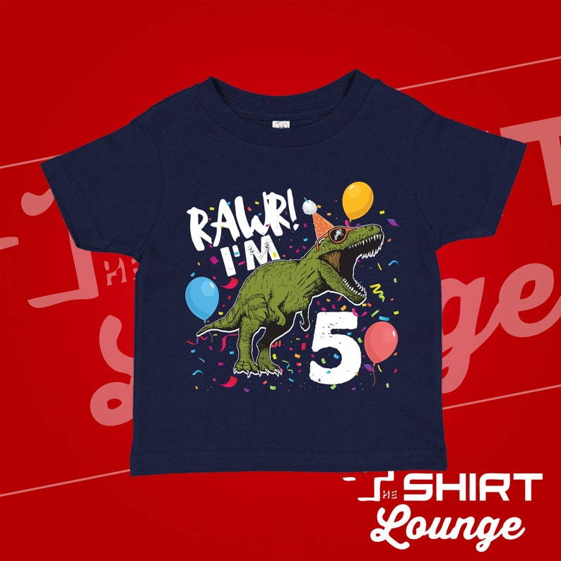 May include: A navy blue t-shirt with a green dinosaur wearing a party hat and sunglasses. The dinosaur is surrounded by confetti and balloons. The text "RAWR! I'M 5" is printed on the shirt.