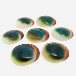 Pode incluir: Sete cabochões ovais e lisos com um gradiente de cores incluindo azul-petróleo profundo, verde-oliva e castanho quente, transitando para uma base branco-creme. Estas peças polidas e arredondadas têm um acabamento brilhante e superfície.