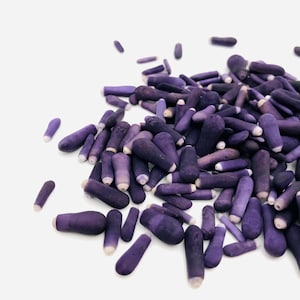 Puede incluir: Un montón grande de pequeñas conchas de mar lisas y alargadas de color púrpura. Las conchas están dispuestas en un patrón aleatorio y todas son aproximadamente del mismo tamaño.