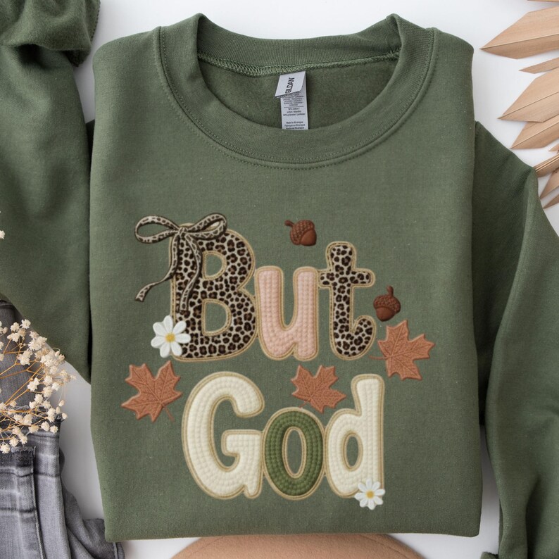 Pu&ograve; includere: Felpa verde oliva con la frase ricamata "But God". La parola "But" presenta un motivo leopardato, con accenti floreali e di foglie. La felpa ha un girocollo e maniche lunghe.