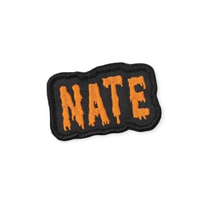 May include: Black embroidered patch with the name "NATE" in orange, stylized with a dripping effect. The patch has a black border and is likely designed to be sewn or ironed onto clothing or accessories.