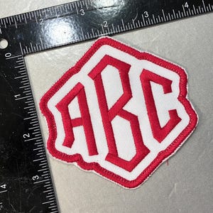 May include: A white fabric patch with red embroidered letters spelling "ARC" in a bold, blocky font. The patch has a red border and a slightly irregular shape.