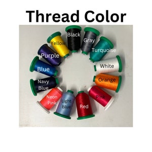 Peut inclure: Un assortiment de bobines de fil de diff&eacute;rentes couleurs, notamment noir, gris, jaune, turquoise, violet, bleu, bleu marine, blanc, orange, rose fluo, bleu clair, rouge et rose. Les bobines sont dispos&eacute;es en cercle sur une surface blanche. Le texte "Thread Color" est &eacute;crit au-dessus des bobines.