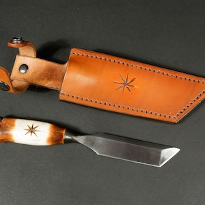 Puede incluir: Una funda de cuero marrón con un diseño de estrella y un pequeño cincel de mango de madera con un diseño de estrella en el mango.