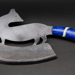 Può includere: Un grande coltello da macellaio in acciaio inossidabile curvo con un manico a motivo blu e bianco. La lama ha la forma di un animale, forse una volpe, con un design ritagliato.