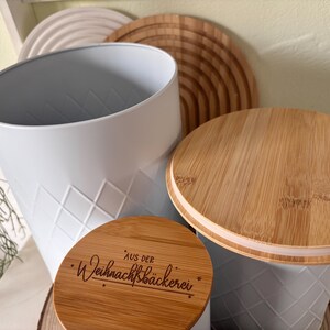 May include: A white metal container with a diamond pattern, paired with a wooden lid. The lid has a natural wood grain finish. A smaller wooden lid with text is also visible. The theme appears to be kitchen storage.