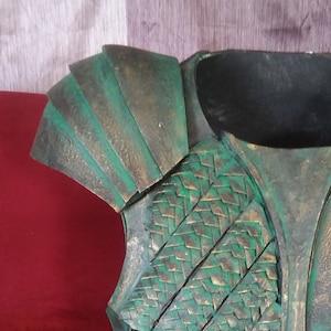 May include: A green and gold metal armor costume piece with a scale-like design. The armor is made of multiple pieces that are joined together.