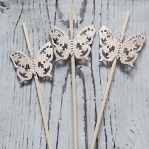 May include: Three silver glitter butterfly cupcake toppers on wooden sticks.