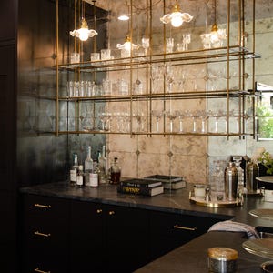 May include: A black kitchen with a bar area featuring a mirrored backsplash with gold shelves and hanging glass lights. The shelves are filled with glassware and bottles. The countertop is black granite with a gold bar rail. The bar area is decorated with a book titled "Wine".