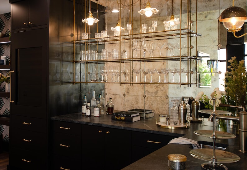 May include: A black kitchen with a bar area featuring a mirrored backsplash with gold shelves and hanging glass lights. The shelves are filled with glassware and bottles. The countertop is black granite with a gold bar rail. The bar area is decorated with a book titled "Wine".