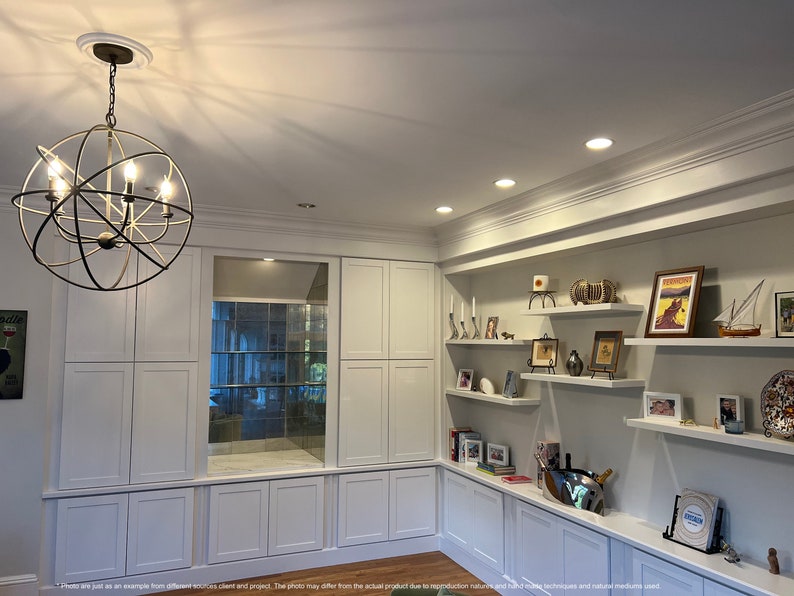 May include: A white built-in shelving unit with a mirrored back and open shelves. The shelves are decorated with framed photos, candles, and decorative items. A globe-shaped chandelier hangs from the ceiling above the unit.