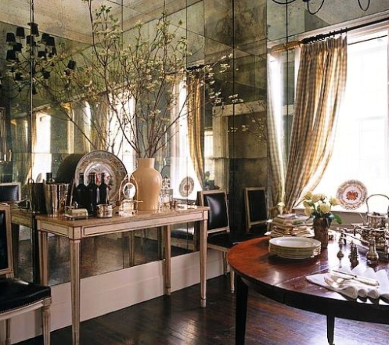 May include: A dining room with a large mirrored wall, a wooden table with chairs, and a white console table with decorative items. The room is decorated with a large bouquet of branches in a vase.