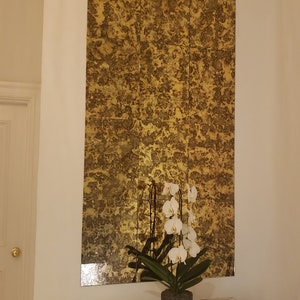 K&ouml;nnte beinhalten: Ein goldfarbener Spiegel mit einer abgenutzten Oberfl&auml;che ist an einer wei&szlig;en Wand &uuml;ber einem Glastisch montiert. Eine wei&szlig;e Orchideenpflanze in einem grauen Topf steht auf dem Tisch, zusammen mit zwei wei&szlig;en rechteckigen Boxen.