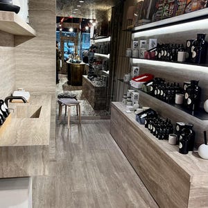 May include: A modern retail store interior with a tiled floor and shelves stocked with various products, including bottles of essential oils and candles. The shelves are lit with LED lights, and the store has a minimalist aesthetic.