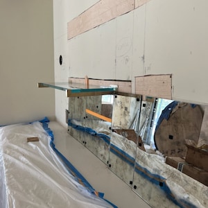 Puede incluir: Una pared blanca con un estante de vidrio y varios espejos unidos a ella. Los espejos est&aacute;n ligeramente envejecidos y tienen un tono azul. La pared est&aacute; cubierta con una lona de pl&aacute;stico blanca.