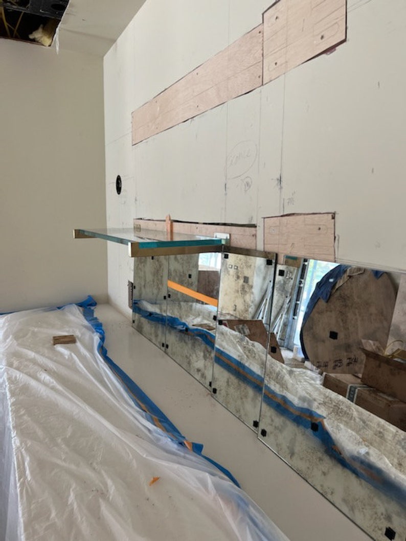 Puede incluir: Una pared blanca con un estante de vidrio y varios espejos unidos a ella. Los espejos est&aacute;n ligeramente envejecidos y tienen un tono azul. La pared est&aacute; cubierta con una lona de pl&aacute;stico blanca.