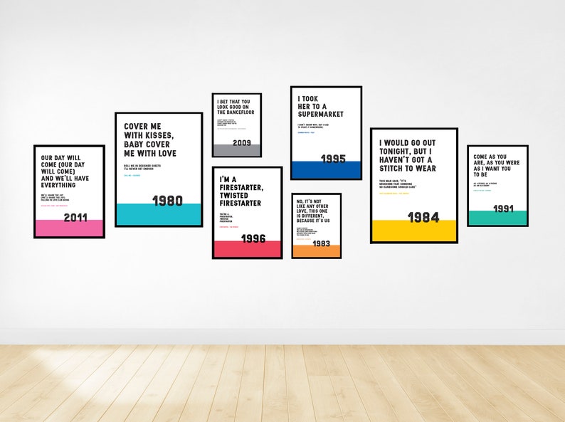 Puede incluir: Una pared blanca con nueve carteles enmarcados, cada uno con una letra de canci&oacute;n diferente y el a&ntilde;o en que se public&oacute;. Los carteles son de varios colores, incluyendo rosa, azul, amarillo y verde.