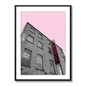 Può includere: Una fotografia in bianco e nero di un edificio con un cielo rosa sullo sfondo. L'edificio ha un cartello al neon rosso che dice "FREAKY" appeso ad esso.