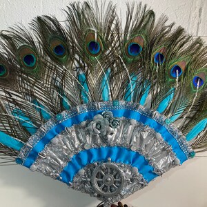 Peut inclure: Une coiffe en plumes de paon avec un &eacute;ventail bleu et argent. L'&eacute;ventail a un motif de roue argent&eacute;e au centre et est d&eacute;cor&eacute; de ruban bleu et argent.