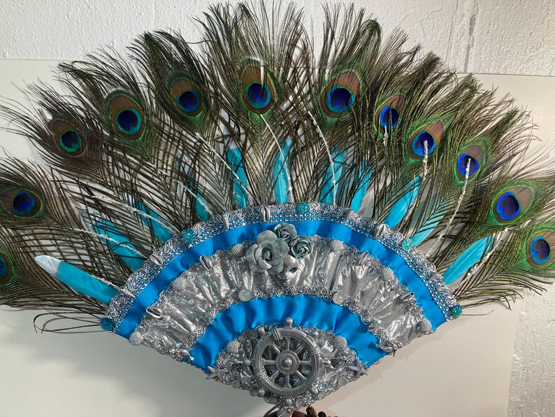 Peut inclure: Une coiffe en plumes de paon avec un &eacute;ventail bleu et argent. L'&eacute;ventail a un motif de roue argent&eacute;e au centre et est d&eacute;cor&eacute; de ruban bleu et argent.