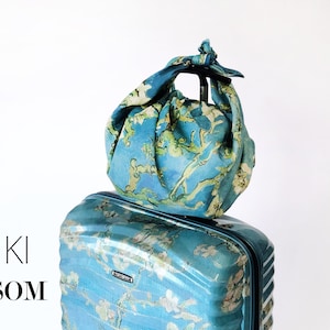 K&ouml;nnte beinhalten: Ein blauer Koffer mit Blumenmuster und eine passende blaue Leinentasche oben drauf. Der Text "LINEN FUROSHIKI ALMOND BLOSSOM" ist auf dem wei&szlig;en Hintergrund gedruckt.