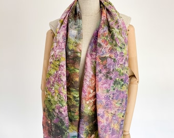 Puede incluir: Una bufanda de seda colorida con un estampado floral en tonos de morado, verde y naranja. La bufanda está drapeada sobre un maniquí.