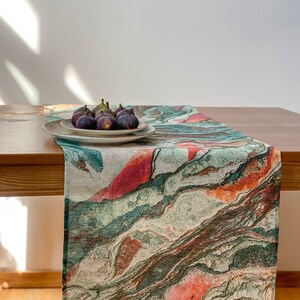 Può includere: Un runner da tavolo in marmo astratto verde, arancione e rosso su un tavolo di legno con un piatto bianco di fichi sopra.