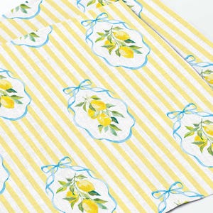 Puede incluir: Tela a rayas amarillas y blancas con un patrón repetido de lazos azules y limones en estilo acuarela.