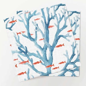 Könnte beinhalten: Ein Set aus drei blauen und weißen Leinen-Servietten mit einem Aquarellmuster aus Korallen und orangefarbenen Fischen.