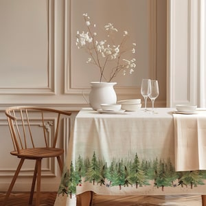 May include: A light-coloured tablecloth featuring a printed watercolour forest of green pine trees along the bottom edge. The table is set with a white ceramic pitcher containing white flowers, white bowls, and two clear stemmed glasses.