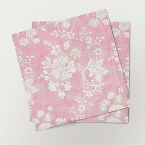May include: Two pink fabric napkins with a white floral pattern. The napkins are folded and stacked on top of each other.