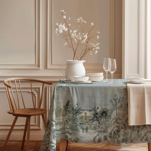 Könnte beinhalten: Ein Esstisch mit einer Tischdecke mit einer Winterszene in Blau und Weiß. Der Tisch ist mit weißem Geschirr, Weingläsern und einer weißen Vase mit weißen Blumen gedeckt. Links steht ein Holzstuhl.