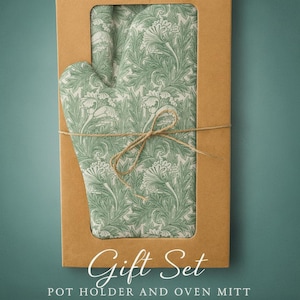 Peut inclure: Un ensemble cadeau comprenant un manique et un gant de cuisine, ornés d'un motif floral vert et blanc. Présenté dans une boîte en carton marron, attaché avec de la ficelle. L'emballage porte les inscriptions "Gift Set" et "POT HOLDER AND OVEN MITT".