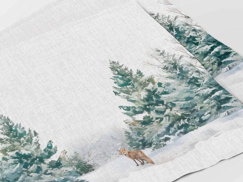 May include: A white linen tea towel with a watercolor design of a snowy forest scene. The design features green pine trees, a red fox, and a white snowy background.