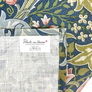 Pu&ograve; includere: Un primo piano di un tessuto di lino bianco con un'etichetta che recita "Prints on linen" e "www.printsonlinen.com". L'etichetta indica anche "Linen 100%" e "Made in Lithuania". Il tessuto presenta un motivo floreale in tonalit&agrave; blu, verde e rosa.