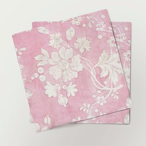 May include: Two pink fabric napkins with a white floral pattern. The napkins are folded and stacked on top of each other.