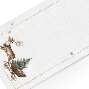 Könnte beinhalten: Weißer Weihnachts-Tischläufer aus Leinen mit festlichem Rentier-Design. Das Rentier zieht einen Schlitten mit einem Weihnachtsbaum. Goldene Sterne und ein goldener Rand ergänzen das festliche Thema.